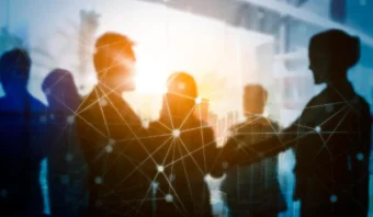 Siluetas de personas dándose la mano en un entorno de oficina, simbolizando el Apoyo y la Networking, con una superposición de red digital y la luz del sol entrando por las ventanas en el fondo.