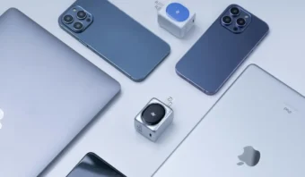 Una disposición plana de dispositivos Apple, incluidos dos iPhones, una MacBook, un iPad y varios cargadores compactos, dispuestos sobre una superficie blanca, perfecta para explorar el significado de la “i” en los productos de Apple.