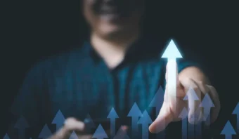 Una persona toca una flecha hacia arriba en una pantalla virtual, con múltiples flechas azules apuntando hacia arriba, simbolizando crecimiento o progreso. ¡Ándale pues!z: el éxito está a solo un toque de distancia.