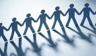 Una fila de figuras recortadas de papel que se toman de la mano y proyectan sombras alargadas sobre una superficie plana simboliza las Relaciones Interpersonales.
