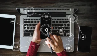 Una persona usa un teléfono inteligente frente a una computadora portátil, con íconos digitales superpuestos, que simbolizan servicios en línea y funciones tecnológicas, perfectos para explorar las netas del marketing digital.