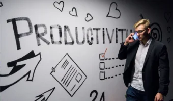 Un hombre vestido de negocios habla por su teléfono mientras está parado junto a una pared con la palabra "PRODUCTIVIDAD", varios garabatos relacionados con el trabajo y notas que abordan los retos de las PyMEs.