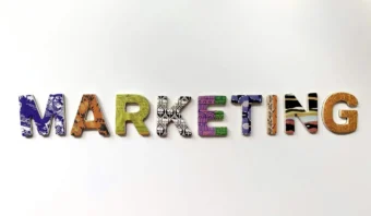 La palabra “MARKETING” está escrita en letras mayúsculas coloridas y estampadas sobre un fondo blanco liso, evocando el toque creativo de un mercadólogo en acción.