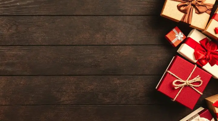 Varias cajas de regalo envueltas con cintas están dispuestas en la esquina superior derecha sobre una superficie de madera oscura, simbolizando promesas cumplidas y dejando la mayor parte de la imagen vacía en el lado izquierdo.