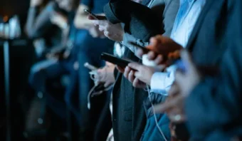 Varias personas vestidas con ropa de trabajo están de pie una al lado de la otra, sosteniendo y usando teléfonos inteligentes mientras interactúan con las redes sociales; sus rostros no son visibles.