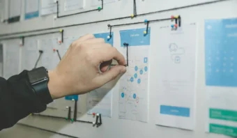 Una persona coloca una cuerda que conecta los wireframes y los bocetos en una pared, delineando el flujo de trabajo de un proyecto o creando un mapa del sistema para el proceso de diseño de una aplicación.