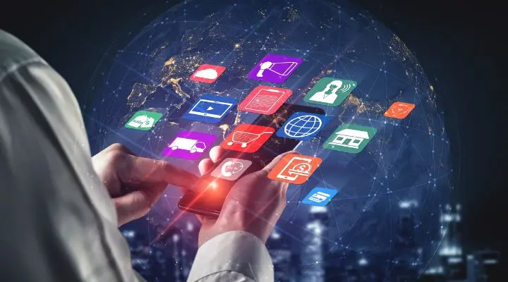 Persona que usa un teléfono inteligente con íconos de aplicaciones coloridos flotando sobre el dispositivo, resaltando canales digitales contra un mapa mundial digital y un fondo del horizonte de la ciudad.