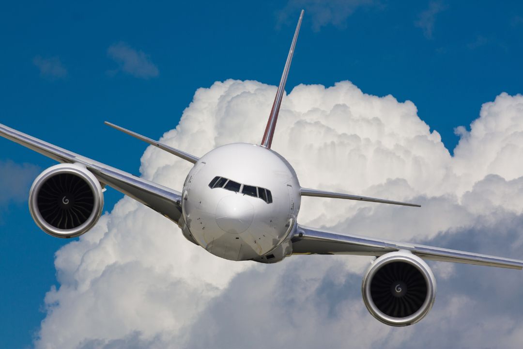 Un avión comercial de oye, Volaris vuela hacia la cámara, enmarcado por grandes nubes en el fondo contra un cielo azul vibrante.