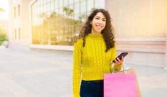 Una mujer joven sosteniendo bolsas de compras y un teléfono celular.