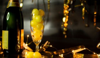 Descripción: Una botella de champagne junto a una copa de uvas.