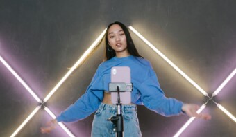 Una chica con un suéter azul parada frente a luces de neón.