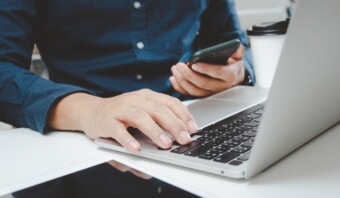 Un hombre realiza múltiples tareas y se dedica a actividades de marketing escribiendo en una computadora portátil y sosteniendo un teléfono celular.