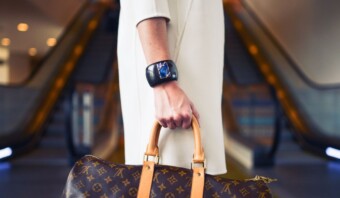 Una mujer que lleva un elegante bolso Louis Vuitton sube con gracia por una escalera mecánica, exudando un aire de lujosa sofisticación.