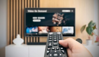 Una mano sosteniendo un control remoto frente a un televisor.