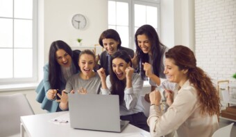 Un grupo de mujeres de negocios se ríen mientras usan una computadora portátil.