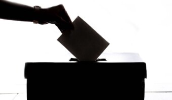 Una mano introduciendo un pedazo de papel en una urna de votación para publicidad oficial.