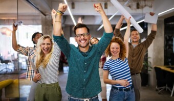 Entusiasta grupo de trabajadores de oficina en una empresa para trabajar celebrando el éxito con papeles y puños levantados en el aire, sonriendo alegremente en un espacio de trabajo moderno.