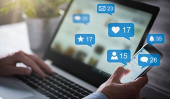 Persona que usa una computadora portátil que muestra íconos internos de participación en las redes sociales, como me gusta, comentarios y recursos compartidos, flotando sobre la pantalla.
