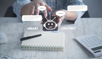 Persona que utiliza un teléfono inteligente con gráficos de chatbot y las palabras "chatbot inteligente" en la pantalla; sobre la mesa hay un bolígrafo y una calculadora, lo que resalta la combinación perfecta de herramientas tradicionales y chatbots de vanguardia.