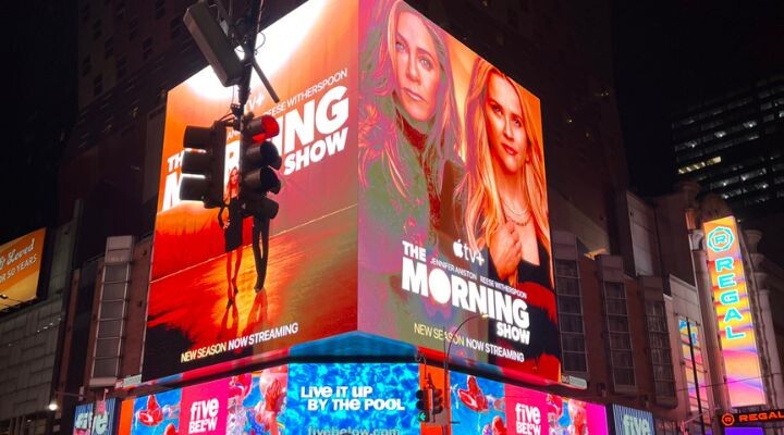Una gran valla publicitaria digital en Times Square, parte del floreciente panorama de los medios DOOH, muestra anuncios de "The Morning Show", con dos mujeres y luces vibrantes y coloridas de los edificios circundantes por la noche.