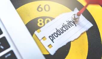 Un primer plano de una hoja de papel con la palabra "productividad" escrita, clavada en un tablón de anuncios, junto al teclado de una computadora portátil.