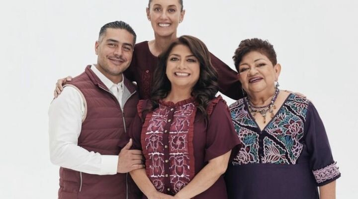 Cuatro adultos, tres mujeres y un hombre, están juntos y sonriendo sobre un fondo blanco liso, todos vistiendo ropa de color granate y morado con patrones bordados, perfecta para una campaña electoral publicitaria antes de las Elecciones 2024.