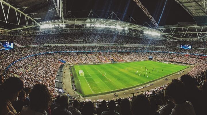 Un estadio grande y repleto de fanáticos viendo un partido de fútbol nocturno en un campo bien iluminado, mostrando la atmósfera vibrante y la publicidad dentro del fútbol mexicano.