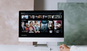 Una persona está usando una computadora que muestra una interfaz de servicio de transmisión. En la pantalla se pueden ver varias miniaturas de programas de televisión y películas, junto con publicidad dirigida en streaming.