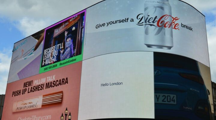 Una gran valla publicitaria digital muestra la innovación con múltiples anuncios, entre ellos una lata de Coca-Cola Light, una máscara de pestañas y el texto "Hola Londres".