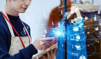 Una persona con delantal usa un teléfono inteligente y una tableta, con íconos de compras digitalizados superpuestos, que representan una combinación de venta minorista tradicional y tecnología digital, resaltando la innovación en las pequeñas empresas.