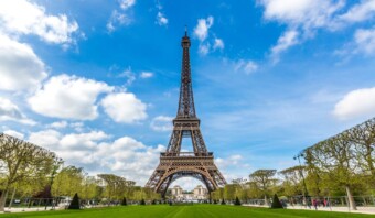 La Torre Eiffel se alza bajo un cielo parcialmente nublado, con césped bien cuidado y árboles que conducen a ella.