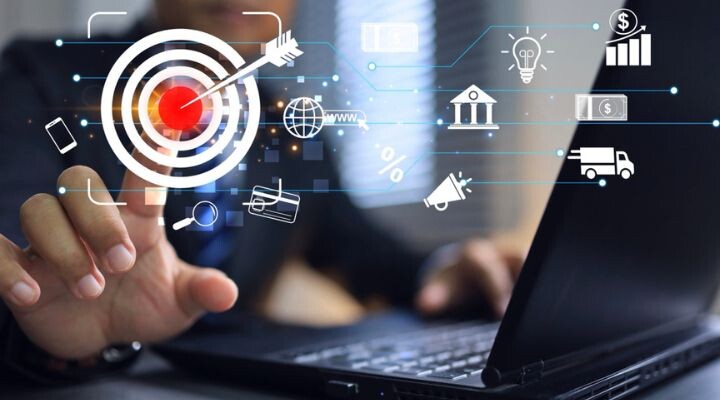 Una persona usa una computadora portátil y apunta a un ícono de objetivo virtual en una pantalla llena de diversos símbolos breves relacionados con negocios y finanzas.