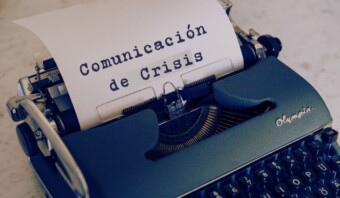 Una máquina de escribir azul sostiene una hoja de papel que dice "Comunicación de Crisis" en español, que se traduce como "Comunicación de Crisis".
