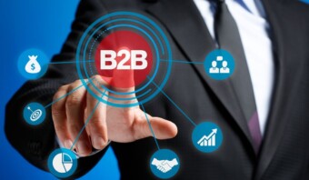 Una persona con traje toca un diagrama que presenta el término "B2B" en el centro, rodeado de varios íconos relacionados con los negocios, como dinero, personas, un apretón de manos y tablas de crecimiento.