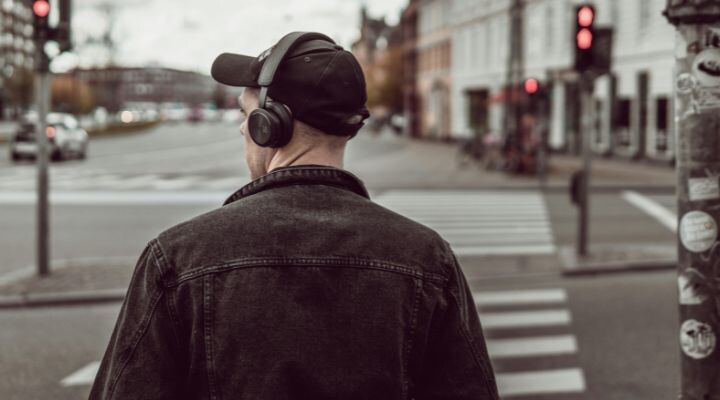 Una persona con auriculares y gorra negra está parada en un cruce peatonal, quizás escuchando publicidad en la radio. El semáforo está en rojo y la calle está vacía.