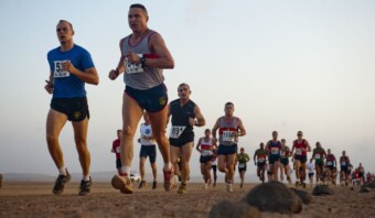 Un grupo de corredores participa en una carrera en un terreno rocoso bajo un cielo nublado. Los corredores llevan dorsales con números y parecen concentrados en el camino que tienen por delante.