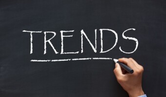 Una mano escribe la palabra "TENDENCIAS" con tiza blanca en una pizarra, subrayándola.