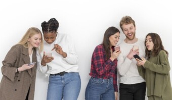 Cinco personas están paradas sobre un fondo blanco, mirando sus teléfonos inteligentes y sonriendo. Parecen estar compartiendo contenido o mostrándose algo interesante en las redes sociales.