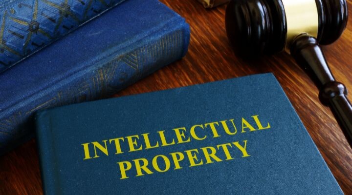 Un libro titulado “Propiedad Intelectual” reposa sobre una mesa de madera al lado de un mazo y otro libro, que profundiza en las invenciones y sus implicaciones legales.