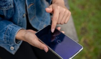 Persona sosteniendo un teléfono inteligente abriendo la aplicación TikTok, con un fondo de césped verde.