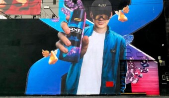 Un mural colorido que presenta a una persona sosteniendo una lata de Axe Blue Lavender, con elementos abstractos y una gran letra "X" en el fondo.