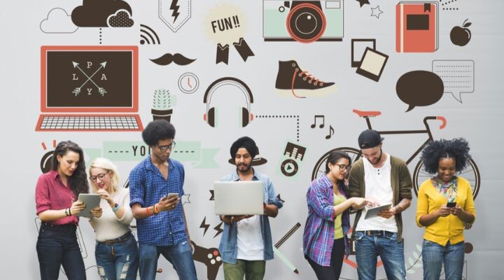 Un grupo diverso de personas, entre las que se incluyen miembros de la Generación Z, se encuentran de pie frente a una pared adornada con íconos coloridos, como una computadora portátil, una cámara y una bicicleta, interactuando activamente con varios dispositivos digitales.