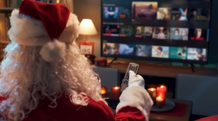 Papá Noel se relaja en fin de año, mirando televisión con un control remoto en la mano, rodeado por el cálido resplandor de las velas encendidas. Es su estrategia de medio tiempo perfecta para relajarse después de una temporada ajetreada.