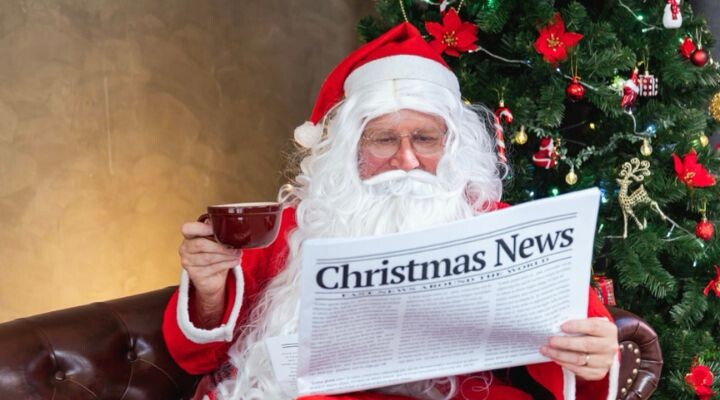 Papá Noel se sienta en un sofá, bebiendo de una taza y leyendo "Noticias de Navidad", mientras las decoraciones de fin de año brillan en el árbol cercano.