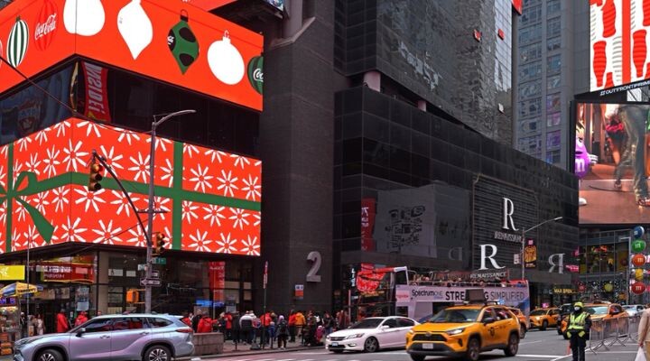 Escena callejera en Times Square llena de taxis amarillos y peatones ansiosos, rodeada de carteles luminosos. Uno presenta un llamativo diseño de papel de regalo rojo, que captura el espíritu festivo de fin de año. La energía vibrante muestra una estrategia de medio emblemática en acción.