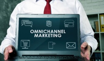 Una persona con camisa blanca y corbata roja sostiene una computadora portátil que muestra el texto "Personalización Omnicanal" junto a íconos relacionados, mostrando el futuro de las estrategias de marketing interconectadas.