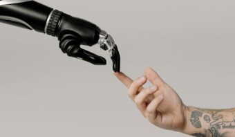 Una mano robótica y una mano humana tocan las puntas de los dedos sobre un fondo liso.