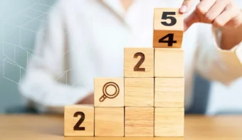 Una persona apila bloques de madera numerados 2, 4 y 5 en orden ascendente. Otro bloque tiene un icono de lupa.