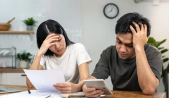 Un hombre y una mujer parecen estresados mientras revisan facturas y usan una calculadora en una mesa, probablemente profundizando en el control de gastos para pymes.