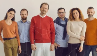 Seis adultos están de pie en fila frente a un fondo claro y sencillo, vestidos con ropa informal en tonos naranja, rojo, azul y beige, y miran a la cámara con expresiones neutrales.